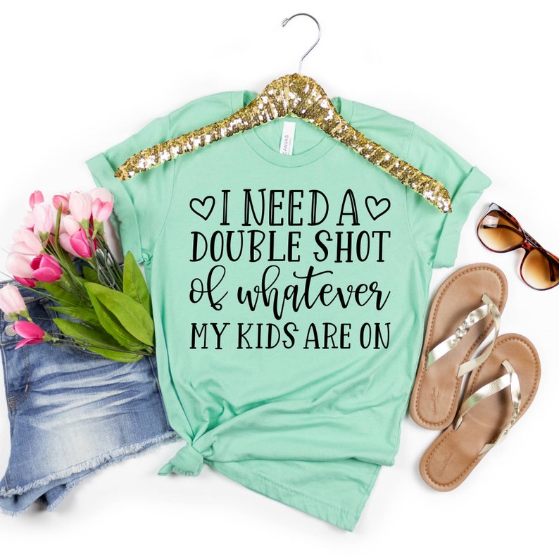 May include: A light green t-shirt with the text "I need a double shot of whatever my kids are on" printed on it. The text is in black and includes two small hearts.