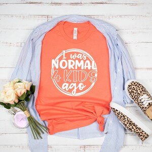 May include: A coral orange t-shirt with white text that reads "I was normal 4 kids ago" in a circle.