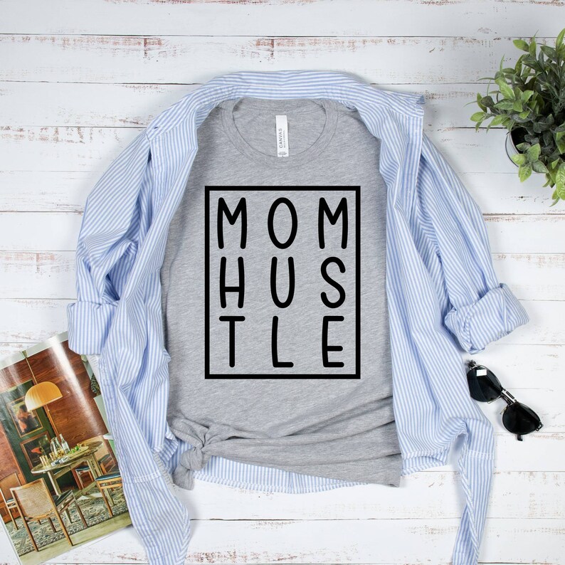 May include: A grey t-shirt with the text "MOM HUSTLE" printed in black within a black square.