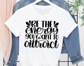 May include: White t-shirt with black text that reads "Be the energy you want to attract".