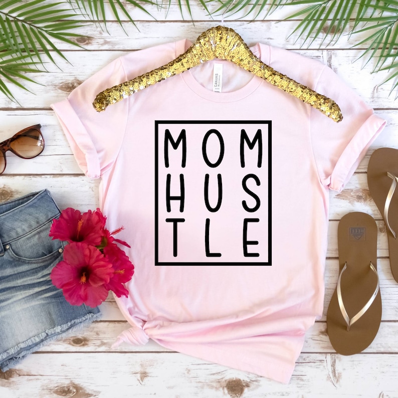 May include: Pink t-shirt with a black square graphic that says "MOM HUSTLE" in block letters.