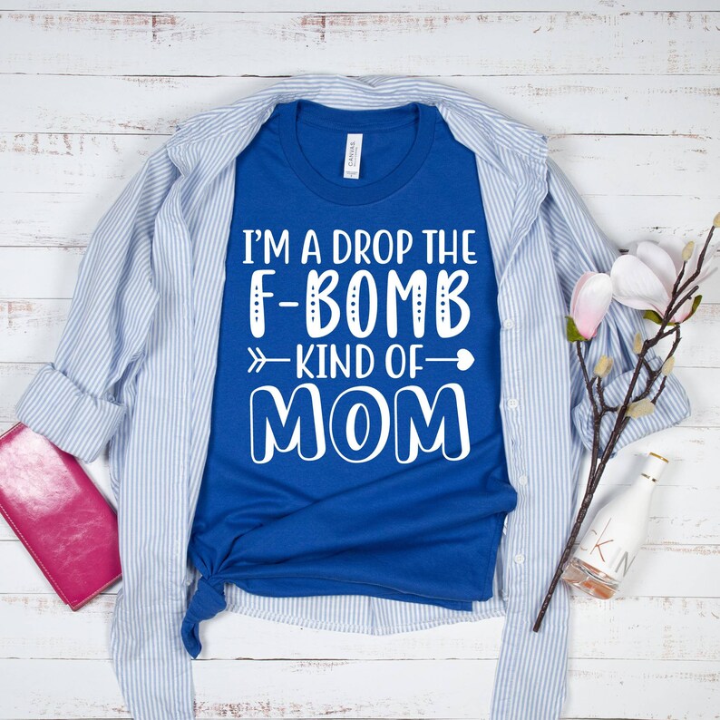 May include: A royal blue t-shirt with white text that reads "I'm a drop the F-bomb kind of mom" with a white arrow pointing to the right and a white heart.