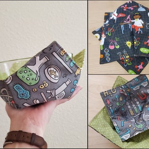 May include: A set of three gray and green fabric bowl cozies with a science theme. The cozies feature a variety of science-related illustrations, including beakers, test tubes, atoms, and molecules. The cozies are perfect for keeping your bowls warm or cold.