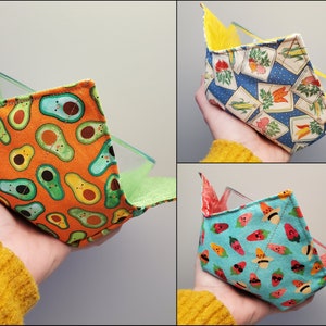 Może przedstawiać: Trzy materiałowe osłonki na miski w różnych wzorach. Pierwsza jest pomarańczowa z zielonymi wzorami awokado. Druga jest niebieska z żółtym, białym i zielonym wzorem kwiatowym. Trzecia jest niebieska z czerwonymi i żółtymi wzorami arbuza.