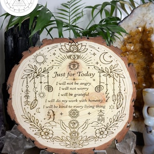 May include: A round wooden plaque with a natural bark edge, engraved with the words "Just for Today" and other text. The design includes floral and celestial motifs, with a wooden stand. The word "PINE" is at the bottom.