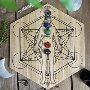 May include: Wooden hexagon-shaped board with a geometric design and a human figure outline. Seven colorful gemstones are placed on the figure, representing the seven chakras.