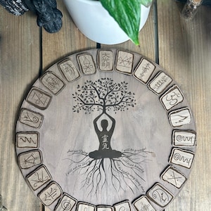 May include: A circular wooden board featuring a tree of life design and a yoga pose silhouette. It has engraved symbols around the edge and the phrases "Just for Today" and "I will be grateful" are inscribed on it.