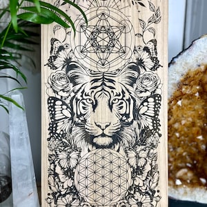 May include: Wooden wall art featuring a detailed black tiger illustration surrounded by butterflies, roses, and geometric patterns. The artwork includes a Metatron's Cube and a Flower of Life design. The piece is displayed on a wooden easel.