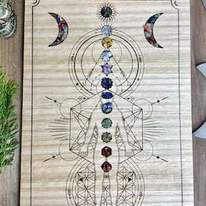 May include: A wooden board with a geometric design and seven cutouts for crystals. The board features a human figure with seven chakras represented by the crystals. The crystals are arranged in a vertical line from the top of the head to the base of the spine. The board is a tool for chakra balancing and meditation.