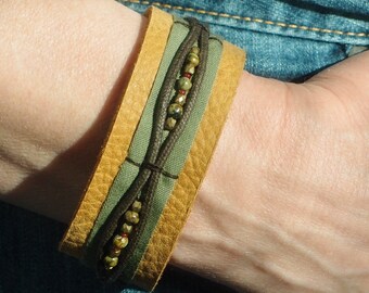 May include: A brown leather bracelet with a green fabric band and a row of colorful beads.