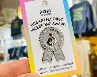 Könnte beinhalten: Eine silberne und goldene Emaille-Anstecknadel mit einem Band. Die Anstecknadel zeigt eine stillende Mutter und den Text "6 MO" auf dem Band. Die Anstecknadel befindet sich auf einer Karte mit dem Text "BREASTFEEDING MILESTONE AWARD" und "SUPPORT. CELEBRATE. NORMALIZE. WWW.ETSY.COM/SHOP/POMSTUDIOS".