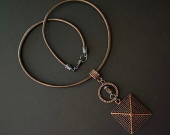 May include: A brown leather choker necklace with a copper pendant featuring a square with a textured surface and a circle with a brown stone.