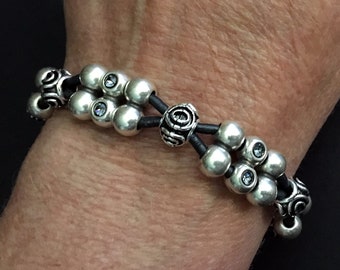 May include: A silver bracelet with black leather cord and silver beads. Some of the beads have small clear crystals.