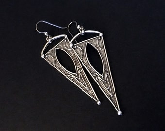 May include: A pair of silver triangle earrings with intricate geometric designs.
