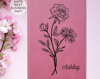 May include: A pink leather journal with a black floral design and the name "Ashley" engraved on the front.
