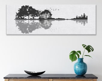 Puede incluir: Impresión en lienzo en blanco y negro de una silueta de guitarra con árboles y un horizonte de ciudad reflejados en el agua. La impresión está colgada en una pared blanca sobre una mesa consola de madera con un jarrón de plantas verdes.