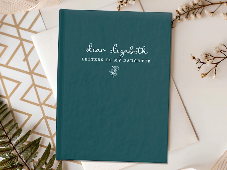 Peut inclure: Un journal de couleur teal avec le texte "dear elizabeth LETTERS TO MY DAUGHTER" en &eacute;criture blanche. Une petite illustration florale est en dessous du texte. Le journal est sur une enveloppe blanche et une surface &agrave; motifs or et blanc.