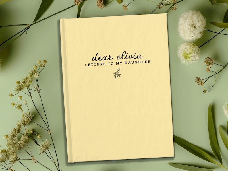 Peut inclure: Un journal cr&egrave;me avec le texte "dear olivia LETTERS TO MY DAUGHTER" en &eacute;criture noire. Une petite illustration florale se trouve sous le texte. Le journal est entour&eacute; de feuillage vert et de fleurs blanches.