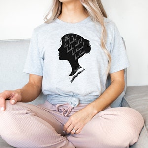 Puede incluir: Una camiseta gris con una silueta negra de la cabeza de una mujer y el texto "She is too fond of books, and has loved her brain" impreso en la parte delantera.