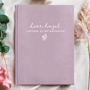 Peut inclure: Un journal de couleur lavande avec le texte "dear hazel LETTERS TO MY DAUGHTER" en &eacute;criture blanche. Une petite illustration florale est en dessous du texte. Le journal est entour&eacute; de fleurs roses et de feuillage vert.