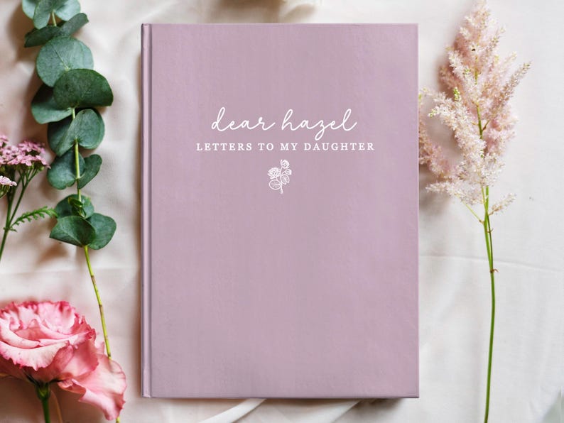 Peut inclure: Un journal de couleur lavande avec le texte "dear hazel LETTERS TO MY DAUGHTER" en &eacute;criture blanche. Une petite illustration florale est en dessous du texte. Le journal est entour&eacute; de fleurs roses et de feuillage vert.