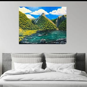 Puede incluir: Una pintura de paisaje representa una cordillera con un lago. La obra presenta un cielo azul vibrante con nubes blancas. Frondosos &aacute;rboles verdes y hierba amarilla rodean el lago, con rocas oscuras en el agua. La pintura se exhibe sobre una cama.