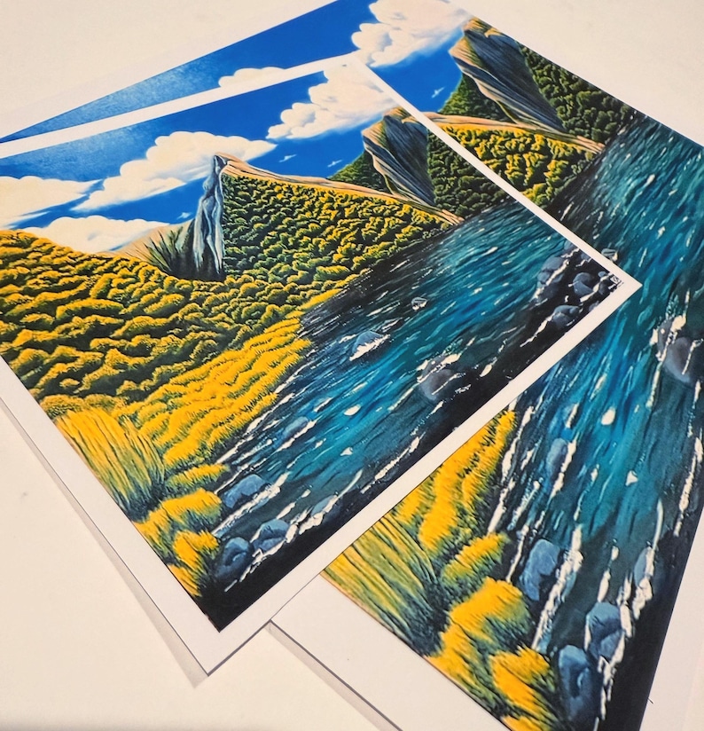 Puede incluir: Tres impresiones art&iacute;sticas que presentan una escena de paisaje vibrante. La obra de arte representa un cielo azul con nubes blancas, una ladera amarilla y verde y un r&iacute;o azul. Las impresiones est&aacute;n sobre papel blanco y se muestran en &aacute;ngulo.