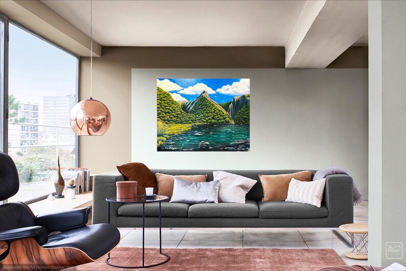 Puede incluir: Una pintura de paisaje representa una cordillera con exuberante vegetaci&oacute;n verde, un lago sereno y un cielo azul brillante con nubes blancas y esponjosas. La obra de arte se exhibe sobre un sof&aacute; gris en una sala de estar moderna.