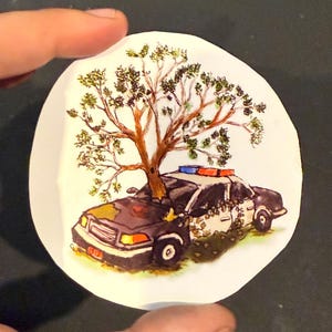 May include: A round, white sticker featuring a watercolor illustration of a police car with a tree growing out of it. The car is black and white with red and blue lights. The tree has brown branches and green leaves.