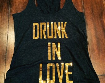May include: A black tank top with gold foil lettering that reads "DRUNK IN LOVE".