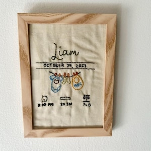 May include: A framed embroidered piece of fabric with the name Liam, the date October 24, 2023, and details about the baby's birth: 8:30 PM, 20 in, 7 lb.