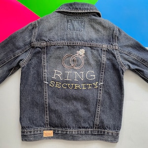 Puede incluir: Una chaqueta vaquera azul oscuro con anillos bordados y el texto "RING SECURITY" en la espalda.