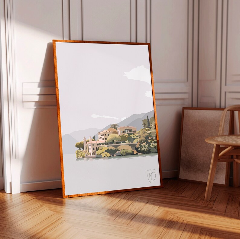 Op de afbeelding: Een ingelijste kunstdruk met een dorpsgezicht aan het meer met gebouwen, bomen en bergen. Het kunstwerk is in een minimalistische stijl met een neutraal kleurenpalet, ingelijst in een houten lijst.