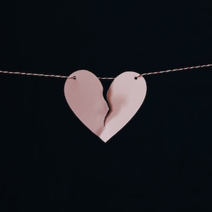 Può includere: Un cuore di carta rosa tagliato a metà è infilato su uno spago rosso e bianco. Il cuore è appeso su uno sfondo nero.