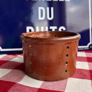 Puede incluir: Una olla de cerámica marrón con agujeros alrededor de los lados. La olla está sentada sobre un mantel a cuadros rojo y blanco.