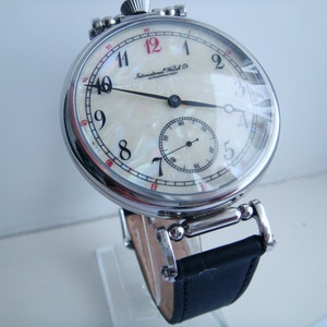 Pode incluir: Um rel&oacute;gio de bolso vintage com mostrador creme e algarismos pretos. O rel&oacute;gio apresenta um pequeno mostrador de segundos e uma bracelete de couro preta. O mostrador do rel&oacute;gio &eacute; protegido por um cristal transparente e a caixa &eacute; de metal polido.