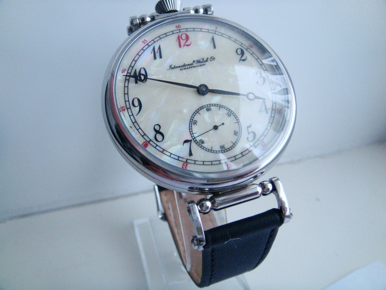 Pode incluir: Um rel&oacute;gio de bolso vintage com mostrador creme e algarismos pretos. O rel&oacute;gio apresenta um pequeno mostrador de segundos e uma bracelete de couro preta. O mostrador do rel&oacute;gio &eacute; protegido por um cristal transparente e a caixa &eacute; de metal polido.