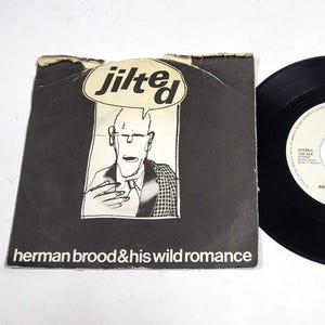 Peut inclure: Un disque vinyle vintage et sa pochette pour "Jilted" de Herman Brood & His Wild Romance. La pochette noire et blanche présente une illustration de dessin animé et le disque est noir avec des étiquettes blanches.