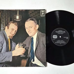 Peut inclure: Album vinyle vintage intitulé "The Best of Mr. Acker Bilk & Bent Fabric". La pochette de l'album présente deux hommes en costume portant des toasts. Un disque vinyle noir est à côté de la pochette.