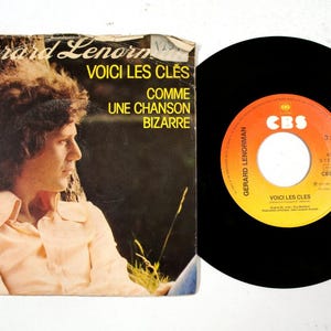 Può includere: Vinile vintage e copertina di Gerard Lenormand. L'etichetta del disco è arancione e bianca con il logo CBS. La copertina presenta il testo "VOICI LES CLÉS" e "COMME UNE CHANSON BIZARRE".
