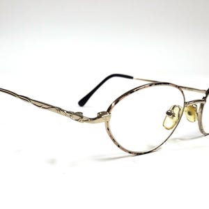 Puede incluir: Gafas de metal doradas con varilla de alambre retorcido y lentes ovaladas.