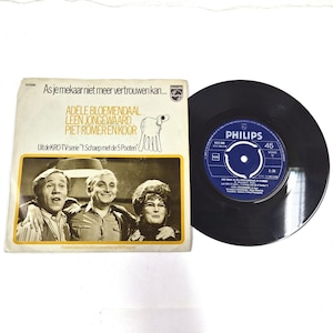 Puede incluir: Un disco de vinilo de 45 RPM de Philips con una funda de papel que incluye el texto As je mekaar niet meer vertrouwen kan, Adele Bloemendaal, Leen Jongewaard, Piet Romer en koor, y Uit de KRO-TV-serie 't Schaep met de 5 Pooten.