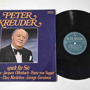 May include: A vintage vinyl record album featuring Peter Kreuder. The album cover is a deep blue with gold lettering and a portrait of Peter Kreuder. The record is black with a teal label.