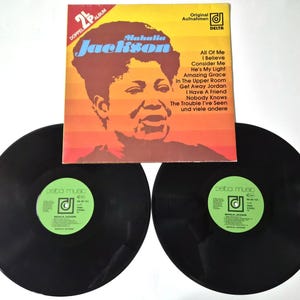 Puede incluir: Un álbum de vinilo vintage de Mahalia Jackson. La portada del álbum es naranja y amarilla con un retrato de Jackson y el título del álbum. Dos discos de vinilo negros son visibles debajo.