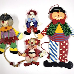 May include: Four wooden puppet clowns with colorful clothing and painted details. The clowns are all different designs and have movable arms and legs.