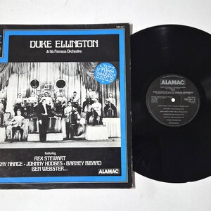 Könnte beinhalten: Ein Vintage-Vinyl-Schallplattenalbum von Duke Ellington and his Famous Orchestra. Das Albumcover zeigt ein schwarz-blaues Design mit einem Foto des Orchesters. Die Schallplatte ist schwarz und glänzend.