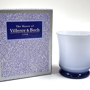 May include: A white ceramic candle holder with a blue rim and base. The candle holder is packaged in a box with a purple and silver design that reads "The House of Villeroy & Boch 1748".