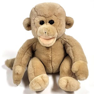 May include: A plush monkey toy in a seated position. The stuffed animal is light brown with a tan face, hands, and feet. It has black eyes and a pink mouth. The monkey's arms and legs are extended.