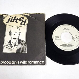 Peut inclure: Un disque vinyle 7 pouces vintage et sa pochette pour Herman Brood & His Wild Romance. La pochette est noire avec le mot "jilted" dans une bulle au-dessus d'une illustration de dessin animé. Le disque est noir avec du texte blanc.