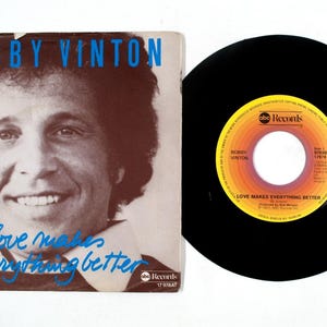 Puede incluir: Un disco de vinilo vintage y su portada con Bobby Vinton. La portada tiene una foto de Bobby Vinton con el texto "BOBBY VINTON" y "Love Makes Everything Better". La etiqueta del disco es naranja y amarilla.